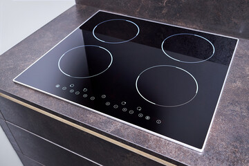 Grey countertop with black glossy built in ceramic glass induction or electric hob stove cooker with four burners in dark empty modern contemporary flat design loft kitchen interior