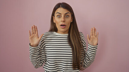 Surprised young hispanic woman with hands raised against a pink isolated background wearing a...