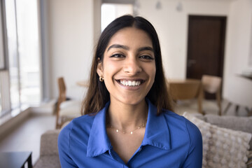 Positive beautiful 20s Indian girl home head shot. Happy young woman looking at camera, showing white teeth in smile, laughing, talking on video call. Conference chat screen shot portrait