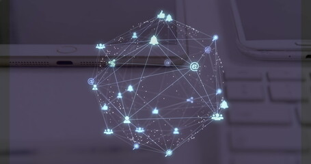 Image of web of connections with icons floating over a desk with a laptop, tablet and smartphone