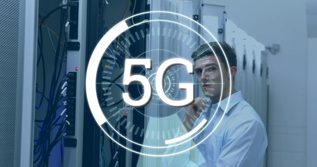 Digital composite of a Caucasian technician looking at a server while futuristic circles around a 5G