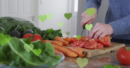 Image of hearts over caucasian man cooking and using tablet