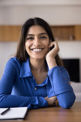 Cheerful beautiful 20s Indian girl student sitting at home workplace table, leaning chin on hand, looking at camera with toothy smile. Happy young freelancer woman vertical head shot portrait - 785309769