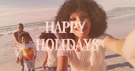 Image of happy holidays text over african american family on the beach