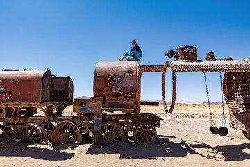 Obraz premium A female tourist is sitting on top of an old train car. Train Cemetery in Uyuni, Bolivia.