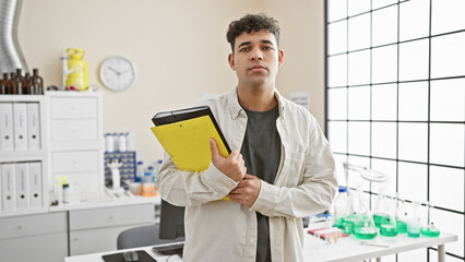 Handsome young man with a clipboard in a science laboratory full of equipment and flasks.