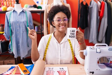 Beautiful african woman with curly hair dressmaker designer drinking from i am the boss cup smiling happy pointing with hand and finger to the side