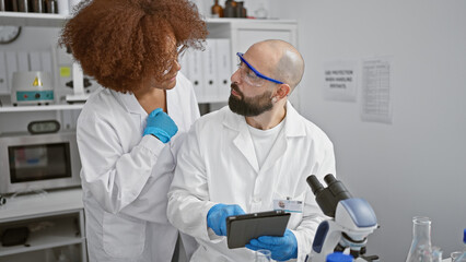 Two dedicated scientists, man and woman, together in the lab performing serious medical research,...