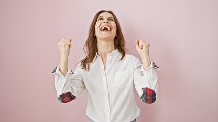 Middle-aged woman celebrating with clenched fists against a pink background, portraying joy and...