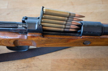 Detail of the insertion of an ammunition clip with 5 30-06 caliber bullets into a Mauser-type bolt-action military rifle on a wooden table