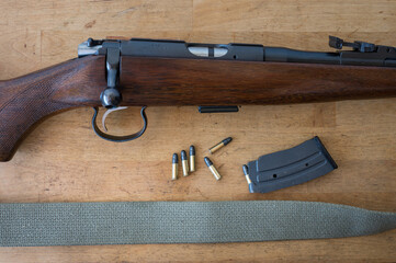 Detail of an old standard .22 caliber bolt action carbine on a wooden table along with bullets and an extended 15 magazine