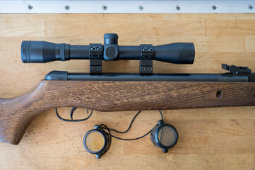 Detail of a light precision air rifle with optical sight on a wooden table. It is a 4.5mm caliber...