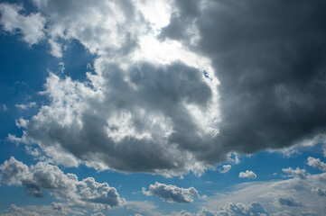 On the blue background of the blue sky with white clouds illuminated by the sun, a strange black...