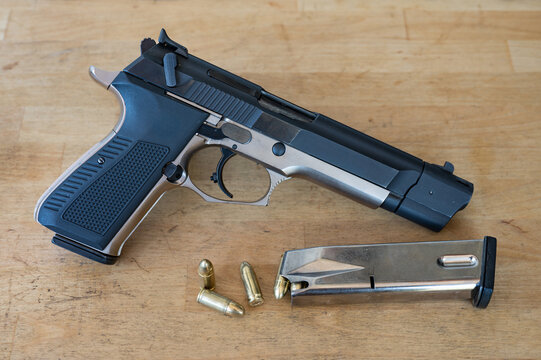 Detail of a nice 9mm police pistol next to a loaded bullet magazine and a few bullets on the wooden table