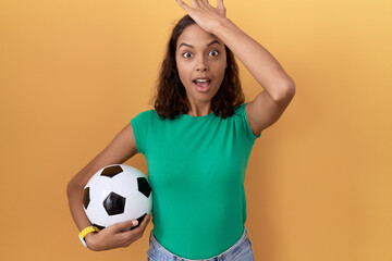 Young hispanic woman holding ball surprised with hand on head for mistake, remember error. forgot,...