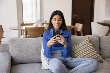 Happy young Indian woman using smart application, service on smartphone for ordering, shopping, typing on mobile phone, smiling, laughing, talking on video call. Front view