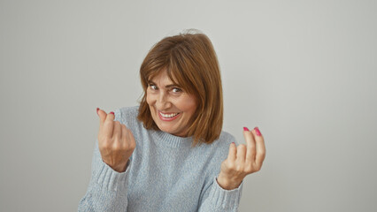 Middle-aged woman making a money gesture against a white wall, implying financial concepts.