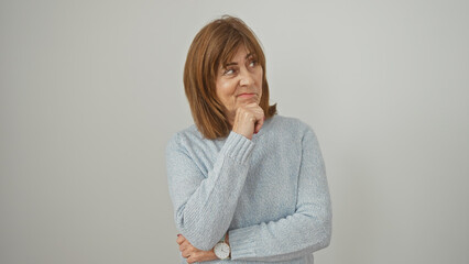 Mature woman in blue sweater contemplating against white background, embodying thoughtfulness and...