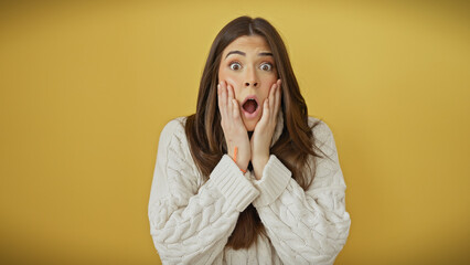 Shocked young hispanic woman with hands on face against a yellow background wearing a white sweater