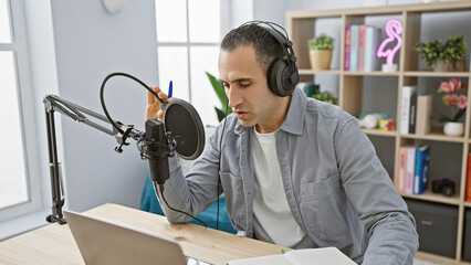 Hispanic man podcasting with microphone and headphones in a home studio setup