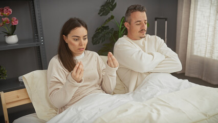 Fototapeta premium A couple exhibits tension while sitting in bed together in a minimalist bedroom, evoking a sense of relationship issues.