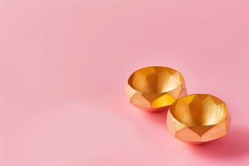 A pair of shiny gold faceted bowls sit on a pink background.