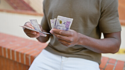 African man counting swedish krona notes on a city street, captured in a focused close-up outdoor...