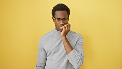 A pensive african american man in glasses stands against a yellow background, evoking thoughtful or...
