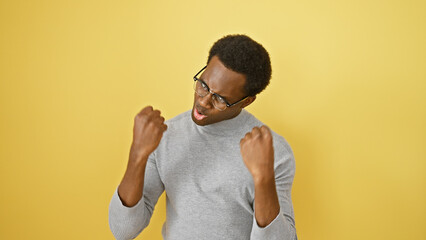 Excited young man in glasses celebrating success against a vibrant yellow background.