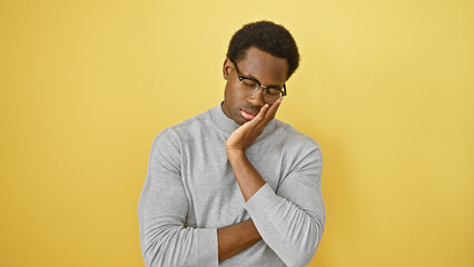 A thoughtful young african american man in glasses isolated against a yellow background.