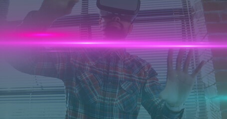 Image of blue and pink light trails moving over biracial man wearing vr headset at office