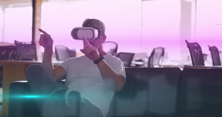 Image of blue and pink light trails moving over caucasian man wearing vr headset at office