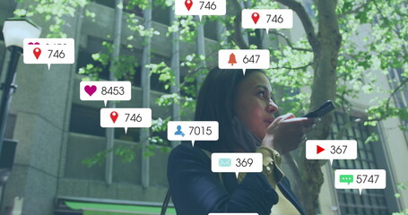 Image of media icons over biracial woman with face mask using smartphone