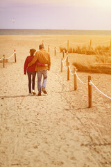 Mature couple in beach sand path walking to the sea at sunset