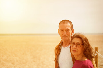 Mature couple smiling at camera in beach at sunset