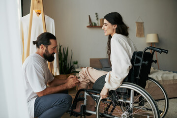 bearded loving man helping his inclusive wife on wheelchair to get dressed while in bedroom