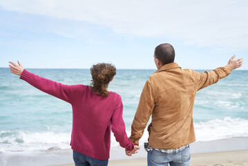 Mature couple waving thieir hands at the beach looking at the ocean