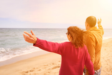 Mature couple waving thieir hands at the beach looking at the ocean at sunset