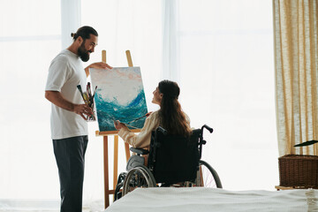 attractive cheerful couple of bearded man and disabled woman painting on easel together at home