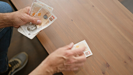 Man exchanges british pounds on a wooden table, depicting a transaction or payment indoors.