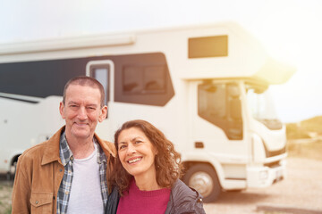 Mature couple smiles to the camera by thier new van at sunset
