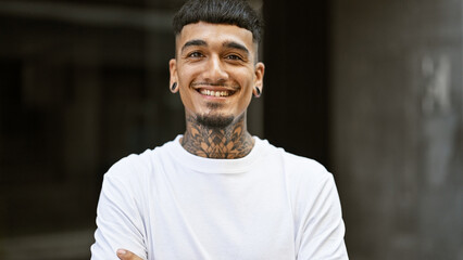 Portrait of a young, confident latin man, smiling with joy and standing on an urban street, exuding...