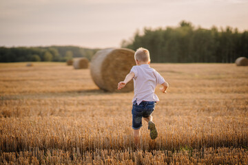 Valmiera, Latvia - August 17, 2024 - A boy runs joyfully across a harvested field with hay bales in...