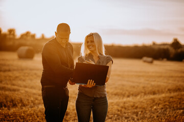 Valmiera, Latvia - August 17, 2024 - Two professionals look at a laptop together in a harvested...