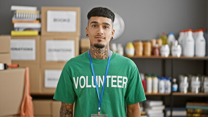 Young latin man volunteering with a serious face, standing resolutely in charity center amid...