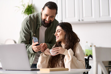 appealing loving couple of bearded man and disabled woman looking at phone in kitchen at home