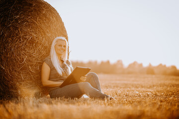 Valmiera, Latvia - August 17, 2024 - .A woman sits leaning against a hay bale in a field, holding a...