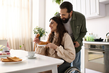 cheerful man having great time at breakfast with his beautiful disabled wife that eating croissant