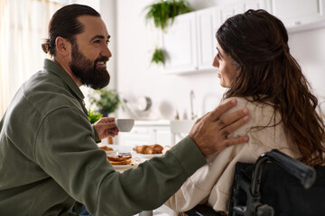 good looking jolly man enjoying breakfast with his disabled merry wife in wheelchair at breakfast