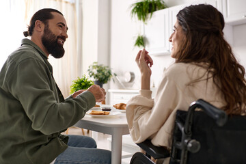 good looking jolly man enjoying breakfast with his disabled merry wife in wheelchair at breakfast